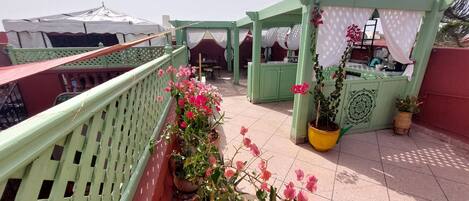 A rooftop terrace with a green railing, potted plants, and a covered seating area.