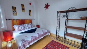 A bedroom with a bed, a red lamp, a shelf unit, and a patterned rug. - Riad Zahrat Al Fajr (El Jadida)