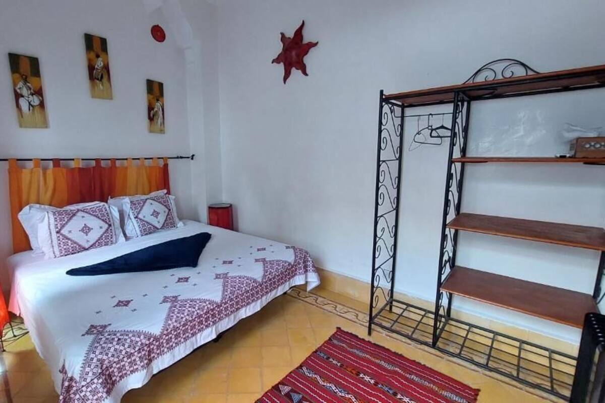 Une chambre à coucher avec un lit, une lampe rouge, une étagère et un tapis à motifs.