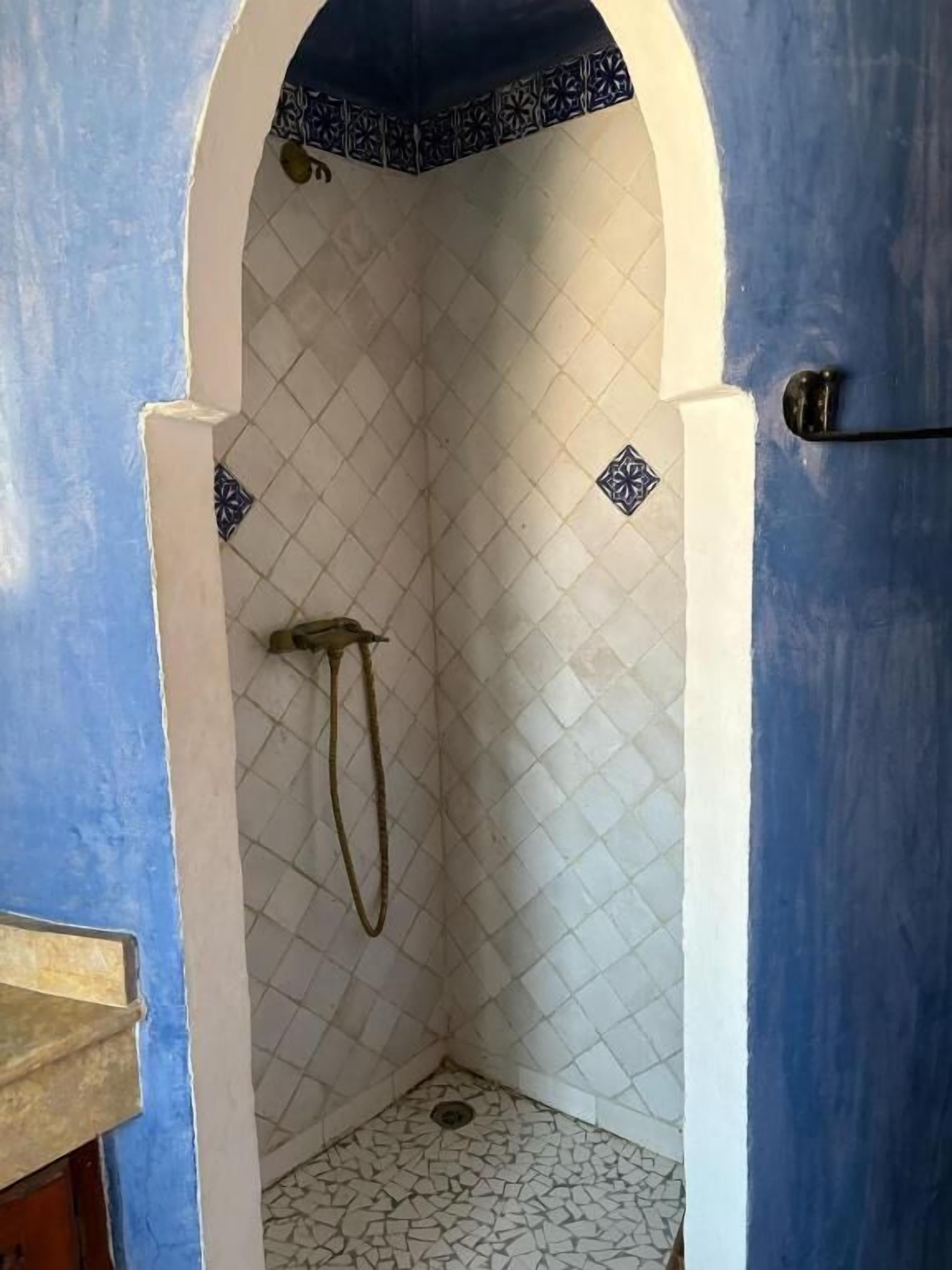 A small, enclosed shower area with a tiled floor and walls, featuring a decorative border at the top of the archway.