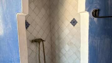A small, enclosed shower area with a tiled floor and walls, featuring a decorative border at the top of the archway.