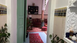 A narrow hallway with a green door, a patterned rug, and a seating area with a red and white patterned sofa and cushions. - Riad Zahrat Al Fajr (El Jadida)