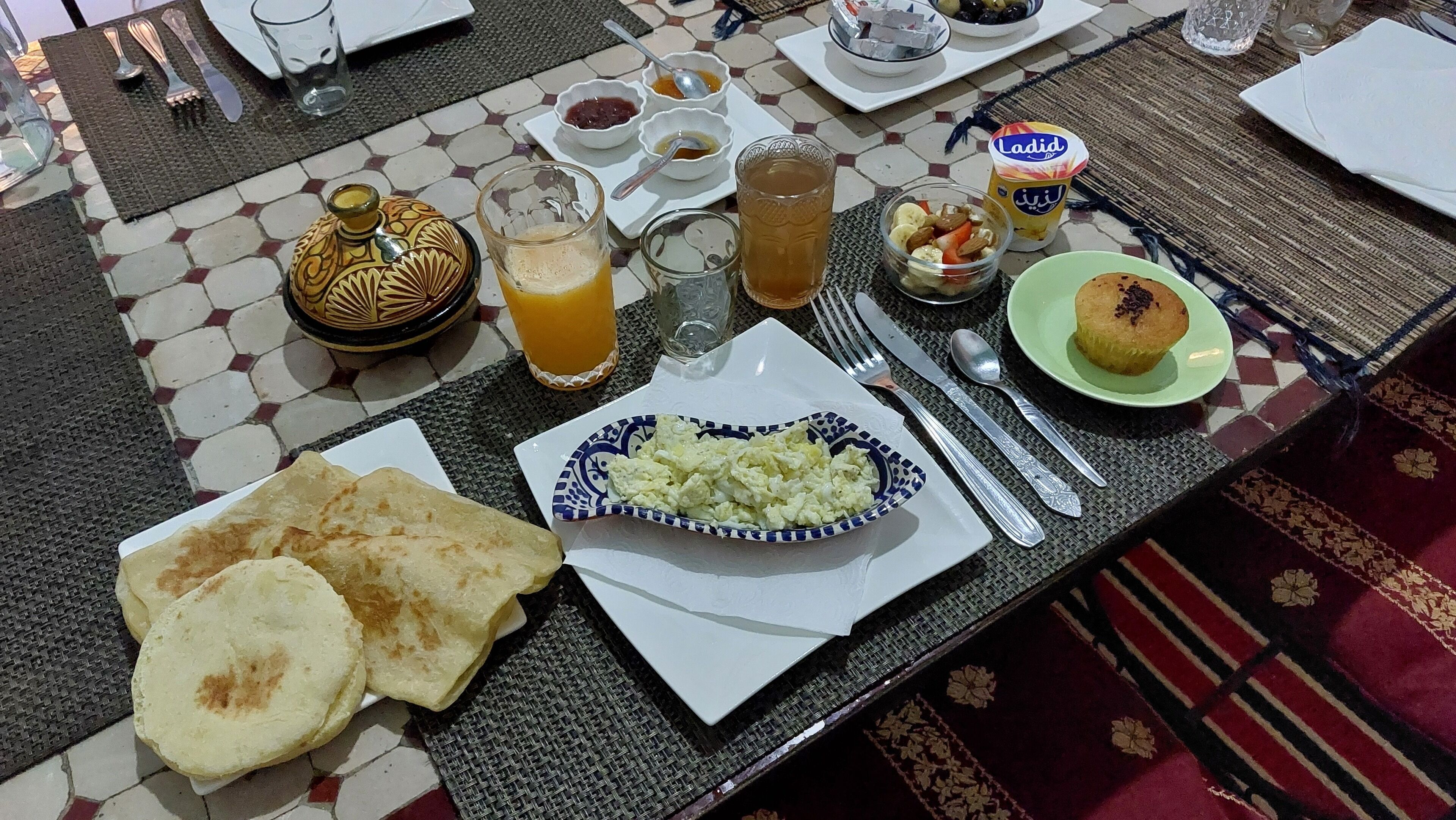 Un desayuno con una variedad de platillos, como pan plano, un tazón de huevos revueltos y un plato de pasteles.
