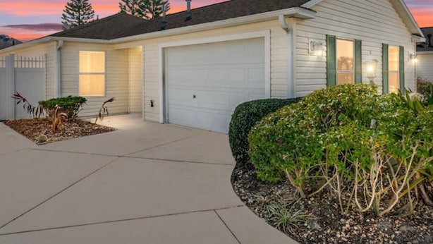 A single-story house with a garage, a driveway, and a well-maintained front yard with shrubs and a small tree. - The Villages FL. Courtyard, Villa House, Golf Cart, Dogs Welcome, Fenced Yard. (The Villages)