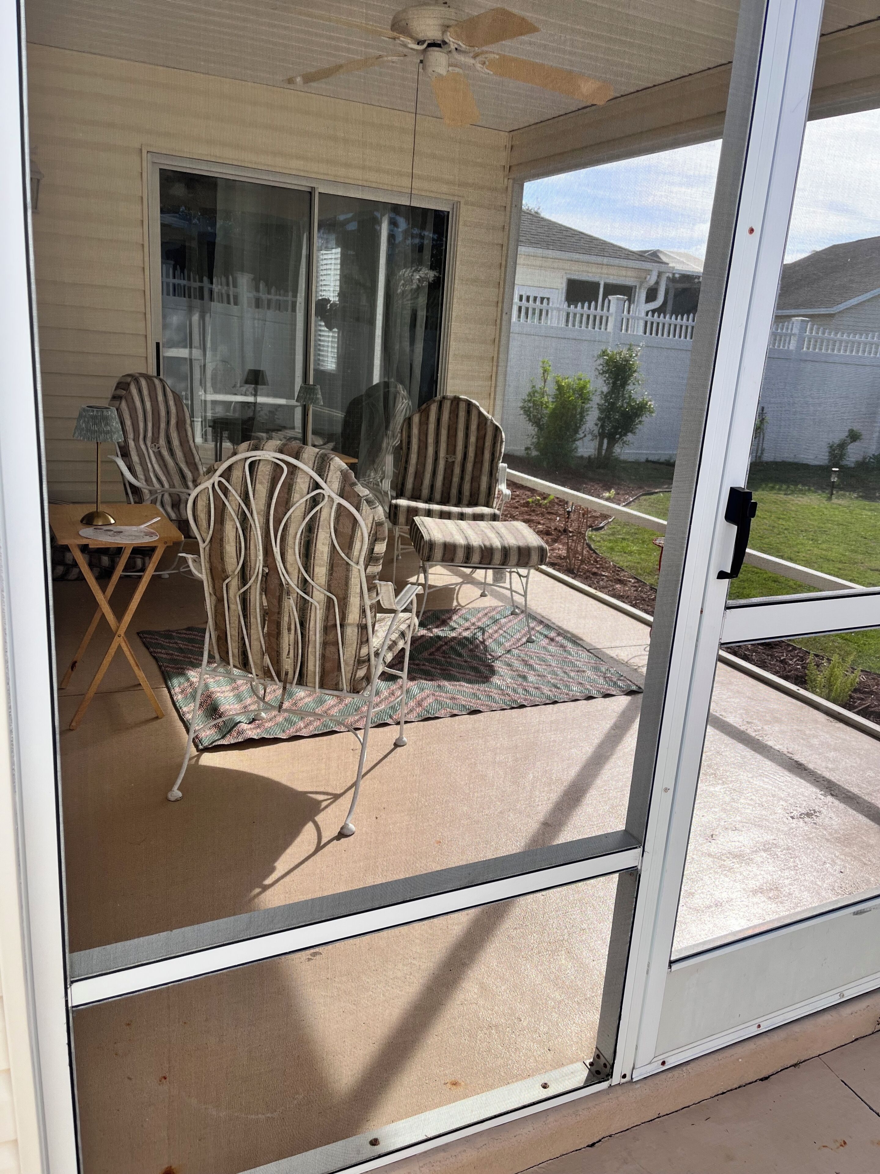 A screened porch with outdoor furniture, a ceiling fan, and a view of a fenced yard.