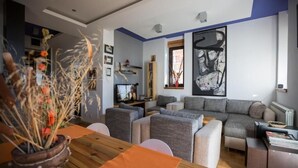 A modern living room with a wooden dining table, grey sofas, and a large abstract painting on the wall. - Vila Plamenac (Divčibare)