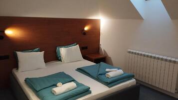 Un dormitorio con techo inclinado, cabecera de madera, dos camas con ropa de cama color turquesa, una mesita de noche y un tragaluz.