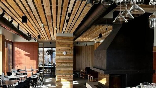 A modern restaurant interior with wooden ceiling beams, a central pillar, and a bar area with glasses. - Vila Plamenac (Divčibare)