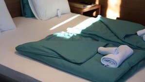 A neatly made bed with a green blanket and a rolled white towel. - Vila Plamenac (Divčibare)