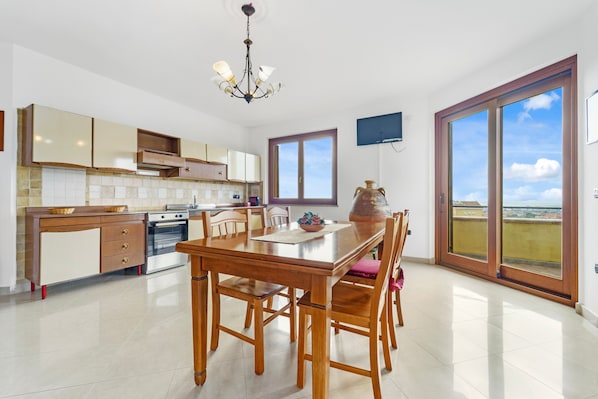 Una cocina con una mesa de comedor, sillas, una araña, armarios y un amplio ventanal con vistas.