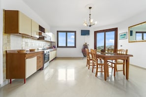 Una cocina con armarios de madera, una mesa de comedor con sillas, una araña y ventanas amplias.