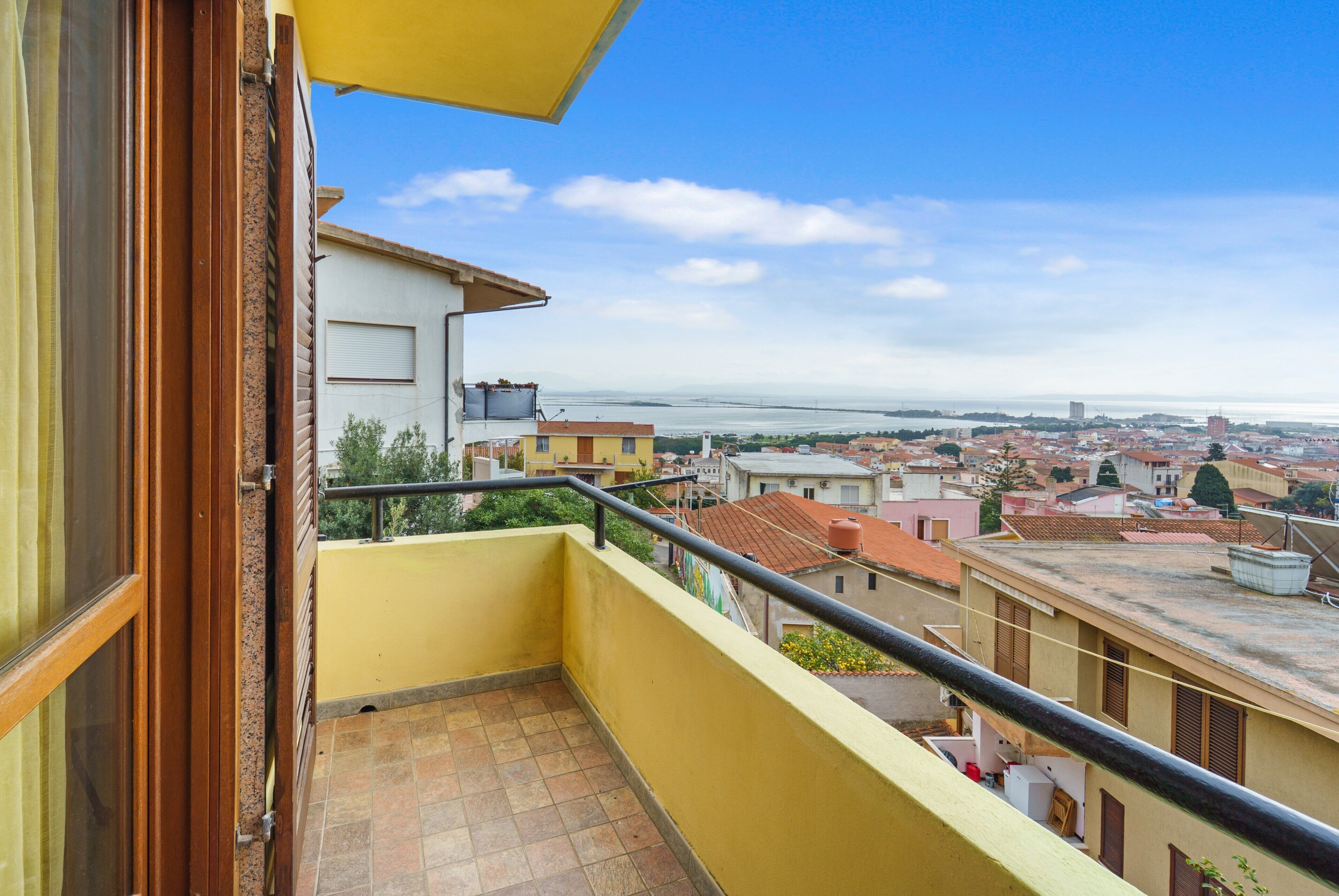 Un balcón con vistas a un paisaje urbano, un edificio de fachada amarilla y un cielo despejado.