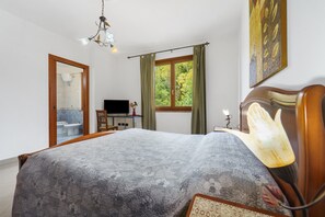 Et soveværelse med seng, skrivebord, stol, fjernsyn og et vindue med gardiner.