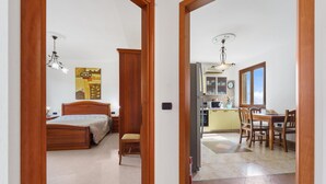 Ein Schlafzimmer mit Bett, Nachttisch und Stuhl, ein Essbereich mit Tisch und Stühlen sowie eine Küchenzeile mit Schränken und einem Kühlschrank.