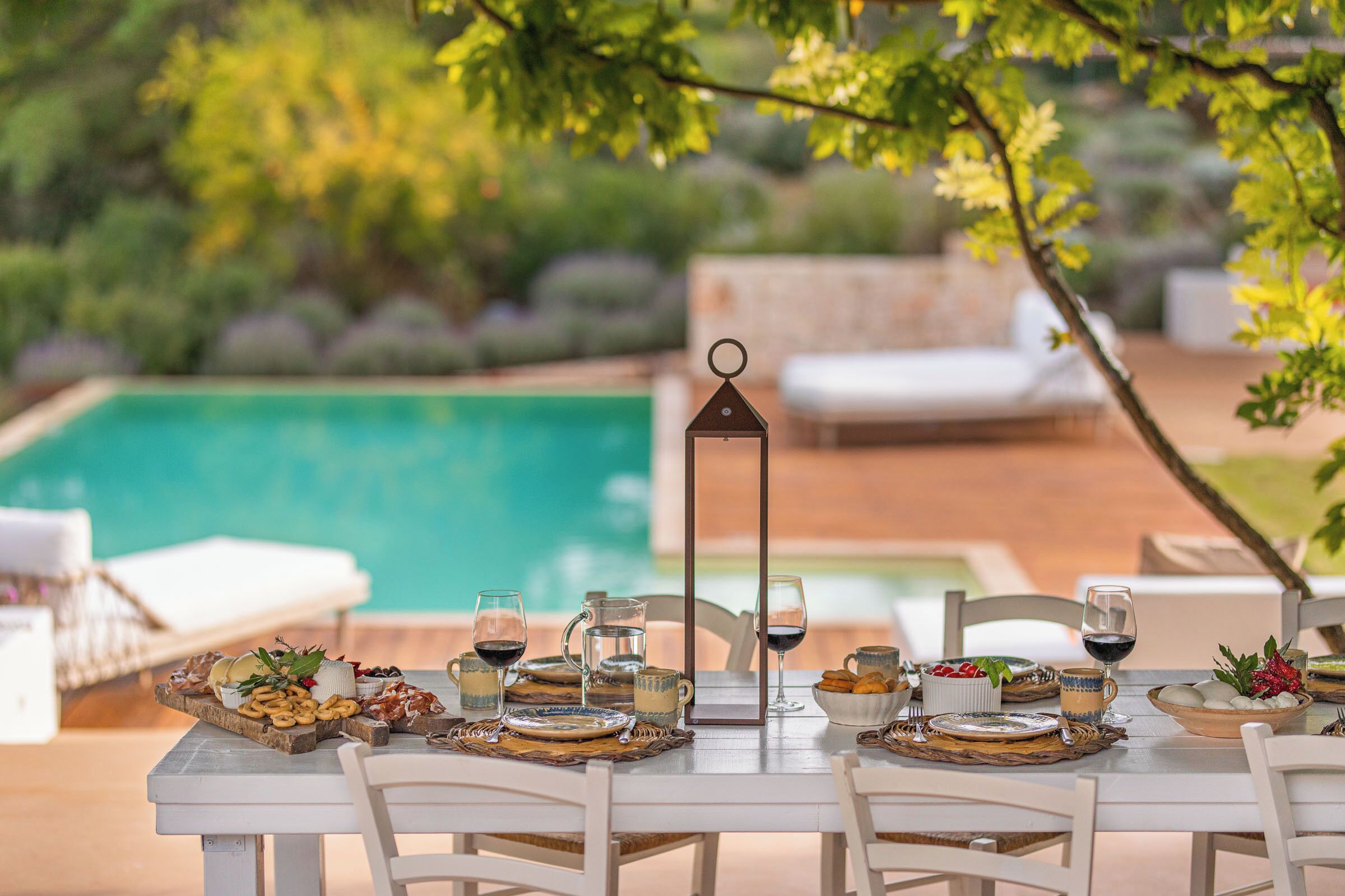 A dining table set outdoors with a pool in the background.