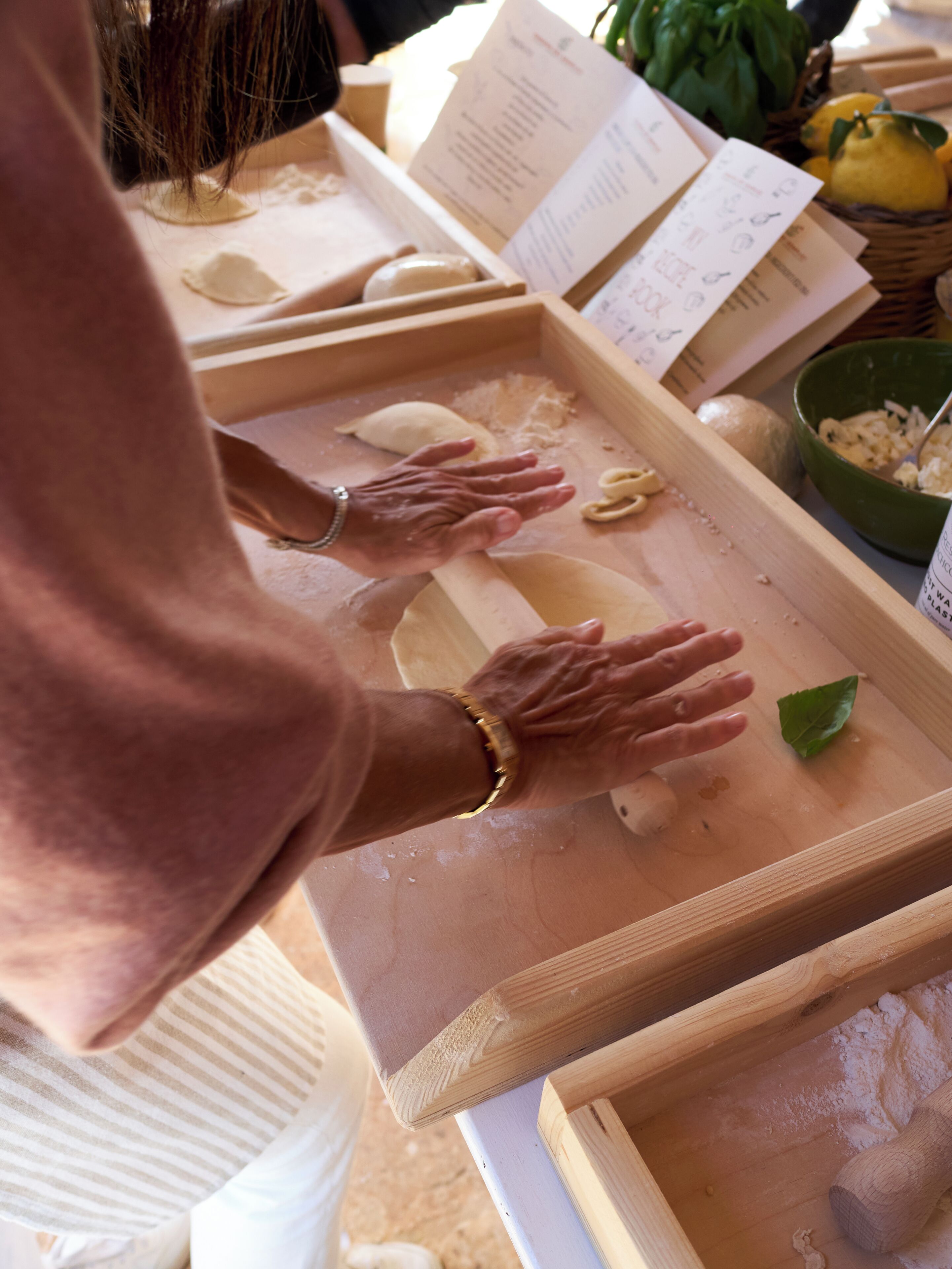 Una persona preparando comida con masa sobre una tabla de madera, rodeada de ingredientes y utensilios.