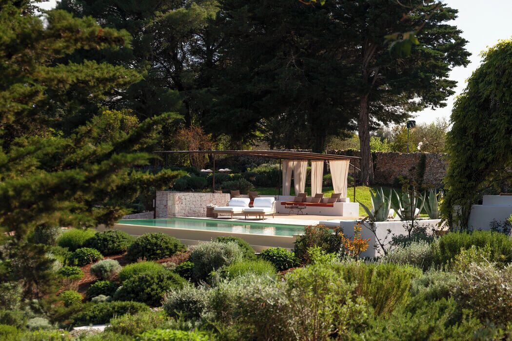 A pool area with lounge chairs, a pergola, and a stone wall.