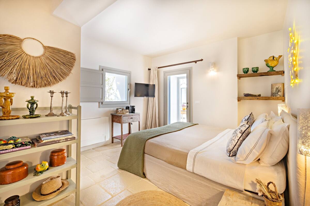A bedroom with a bed, shelves with decorative items, a television, and a window.
