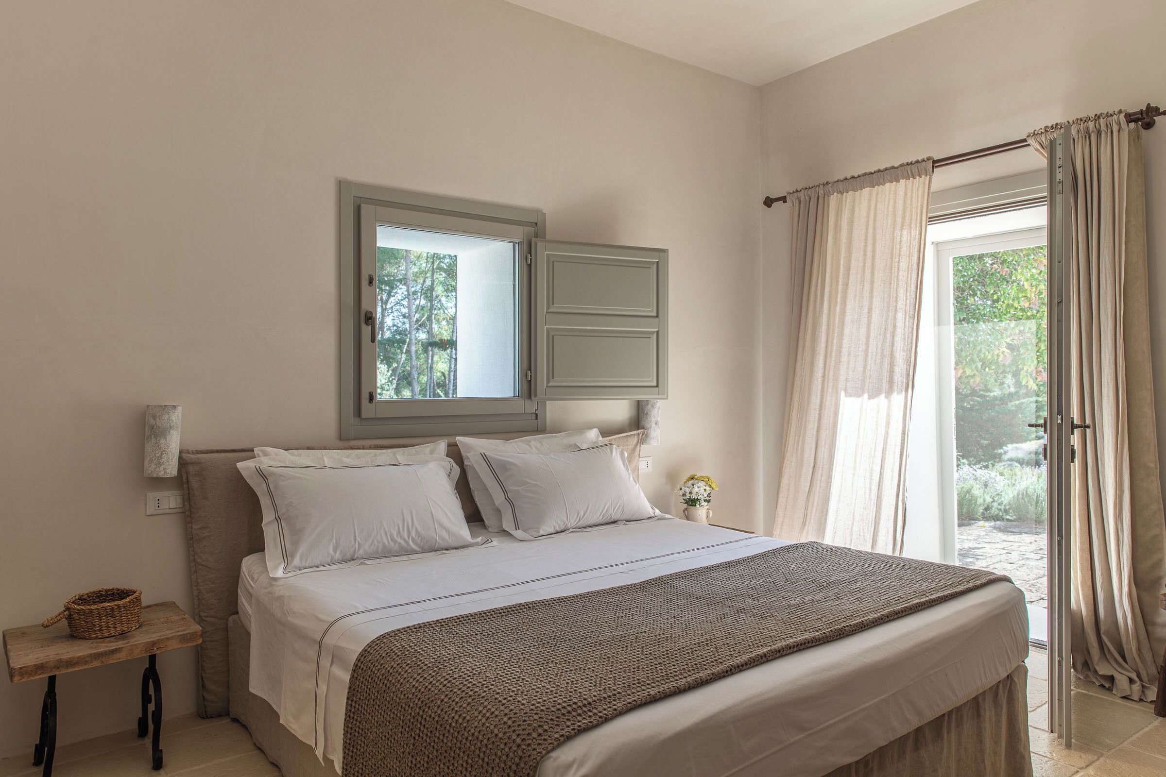 Un dormitorio con una cama, una mesita de noche, una ventana y una puerta que da a un espacio exterior.