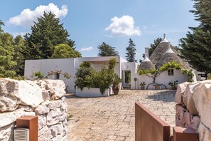 Un patio con muros de piedra, plantas en macetas y un edificio con un techo cónico característico.