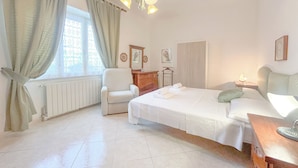 A hotel room with a bed, a chair, a dresser, and a window with curtains. - SV - Moroni (Savona)