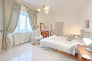 A hotel room with a bed, a chair, a dresser, and a window with curtains. - SV - Moroni (Savona)