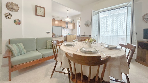 A dining area with a round table set for four, a sofa, and a kitchen in the background. - SV - Moroni (Savona)