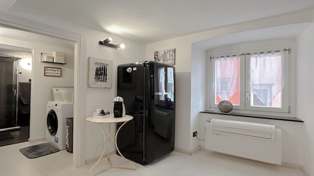 A compact kitchen with a refrigerator, a washing machine, and a small table with a coffee maker. - SV - Pia (Savona)