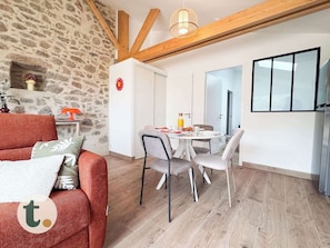 A room with a stone wall, wooden beams, a dining table with chairs, a sofa, and a TV.