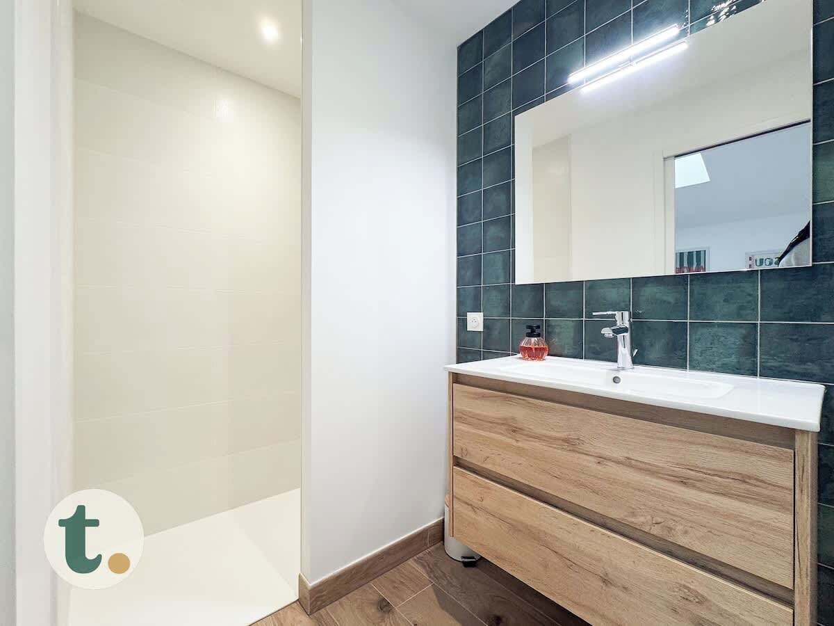 A modern bathroom with a white sink, wooden vanity, and dark green tiles.