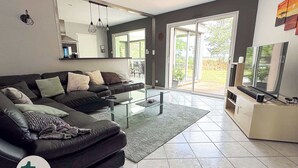 Un salon moderne avec un canapé en cuir noir, une table basse en verre et un téléviseur à écran plat posé sur un meuble.