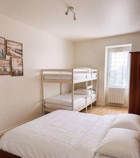 Een kamer met stapelbedden, een groot raam met jaloezieën en een plafondlamp.