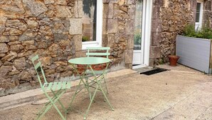 Ein Steinhaus mit einer kleinen Terrasse, zwei Fenstern und einem grünen Klapptisch.