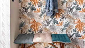 Ein Zimmer mit einem Holz-Kleiderständer, einer Bank mit Kissen und einer Wand mit tropischem Blattmuster.