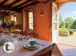 Un coin repas avec une table dressée pour quatre personnes, un vase rempli de fleurs et une vue sur l’extérieur.