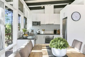 A modern kitchen with white cabinets, a wooden dining table, and a potted plant. - The Moonah Beach Shack (Rye)