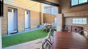Un’area esterna riparata con tavolo e sedie in legno, un piccolo prato e un edificio con rivestimento in legno e una finestra.