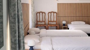 Ein Schlafzimmer mit zwei Betten, Holzstühlen, einem Nachttisch und einem Kopfteil mit vertikalen Linien.