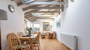Een eethoek met een houten tafel en stoelen, een klok aan de muur, en een raam met natuurlijk licht.