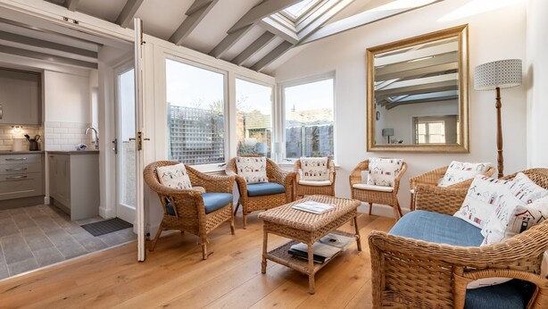 Een gezellige woonkamer met rieten meubels, een grote spiegel en uitzicht op de stad door grote ramen.