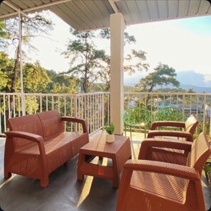 A covered outdoor seating area with wicker furniture and a view of trees and buildings in the background.