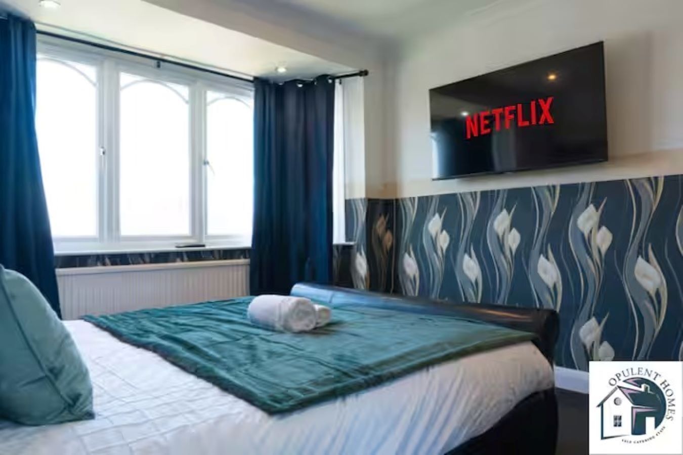 Une chambre d’hôtel avec un lit, un téléviseur fixé au mur et une fenêtre avec des rideaux.