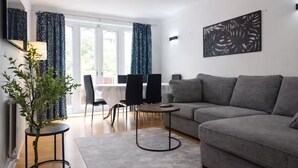 Un saló modern amb un sofà gris, una taula rodona petita i una zona de menjador amb cadires.