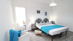 A bedroom with a bed, two bedside tables, a chair, a large window, and a hanging light fixture.