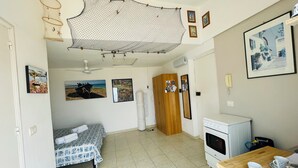 A small, well-lit room with a bed, a desk with a cup and saucer, a white stove, and a ceiling fan. - "La Tonnara" is a studio apartment with a sea view terrace, it is located in the central area (Castellammare del Golfo)