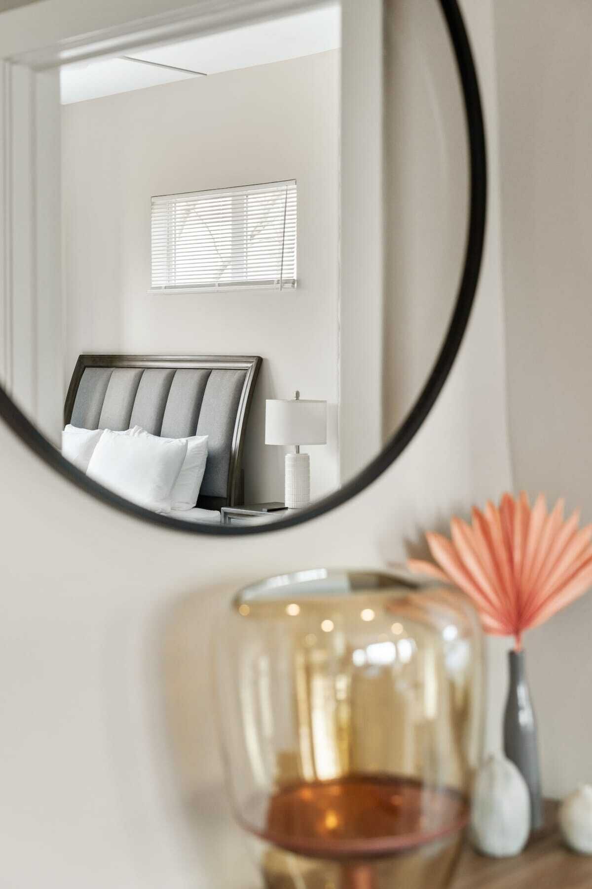 A bedroom with a bed, a bedside table, a lamp, and a mirror reflecting the room.