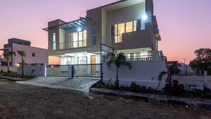 A modern two-story house with a balcony, a gated entrance, and a driveway. - ELIVAAS White House 4BHK Villa With Pool (Igatpuri)