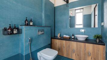 Un baño con pared azul de azulejos, un inodoro blanco, un tocador de madera con lavabo y un espejo.
