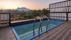 A rooftop pool with metal railings, a view of distant mountains, and a wooden deck. - ELIVAAS White House 4BHK Villa With Pool (Igatpuri)