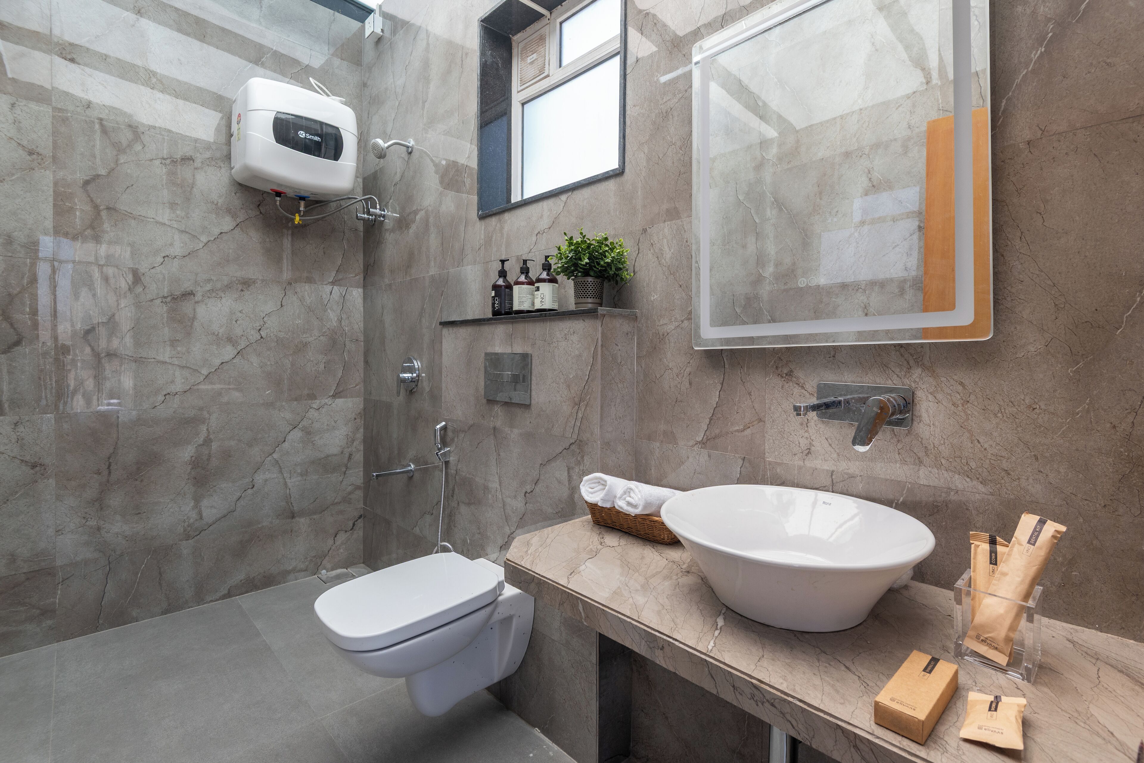 A modern bathroom with a marble wall, a white toilet, a large white sink, and a shower.